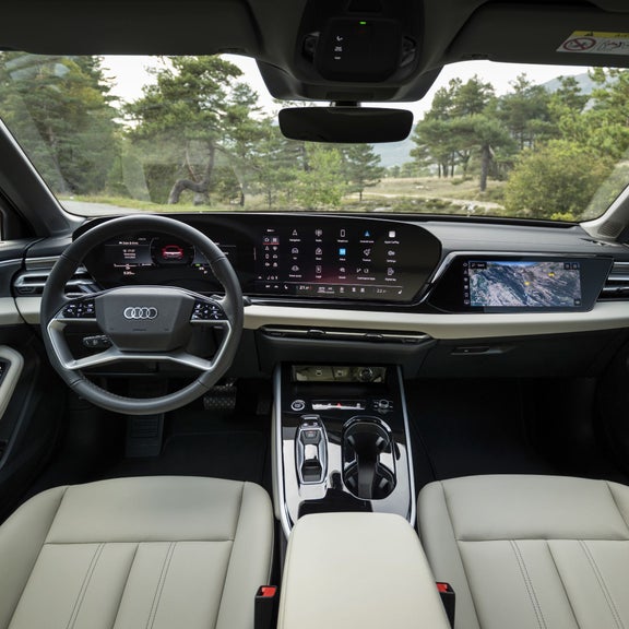 Die Innenansicht eines Audi mit einem modernen, digitalen Cockpit. Das Lenkrad und das Armaturenbrett sind von einem großen, nahtlosen Display begleitet, das verschiedene Fahrzeuginformationen anzeigt. Der Fokus liegt auf den digitalen Steuerungen und der eleganten Ausstattung des Fahrzeuginnenraums.