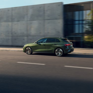 Grüner Audi A3 Sportback fährt auf leerer Straße an einer Betonwand entlang.