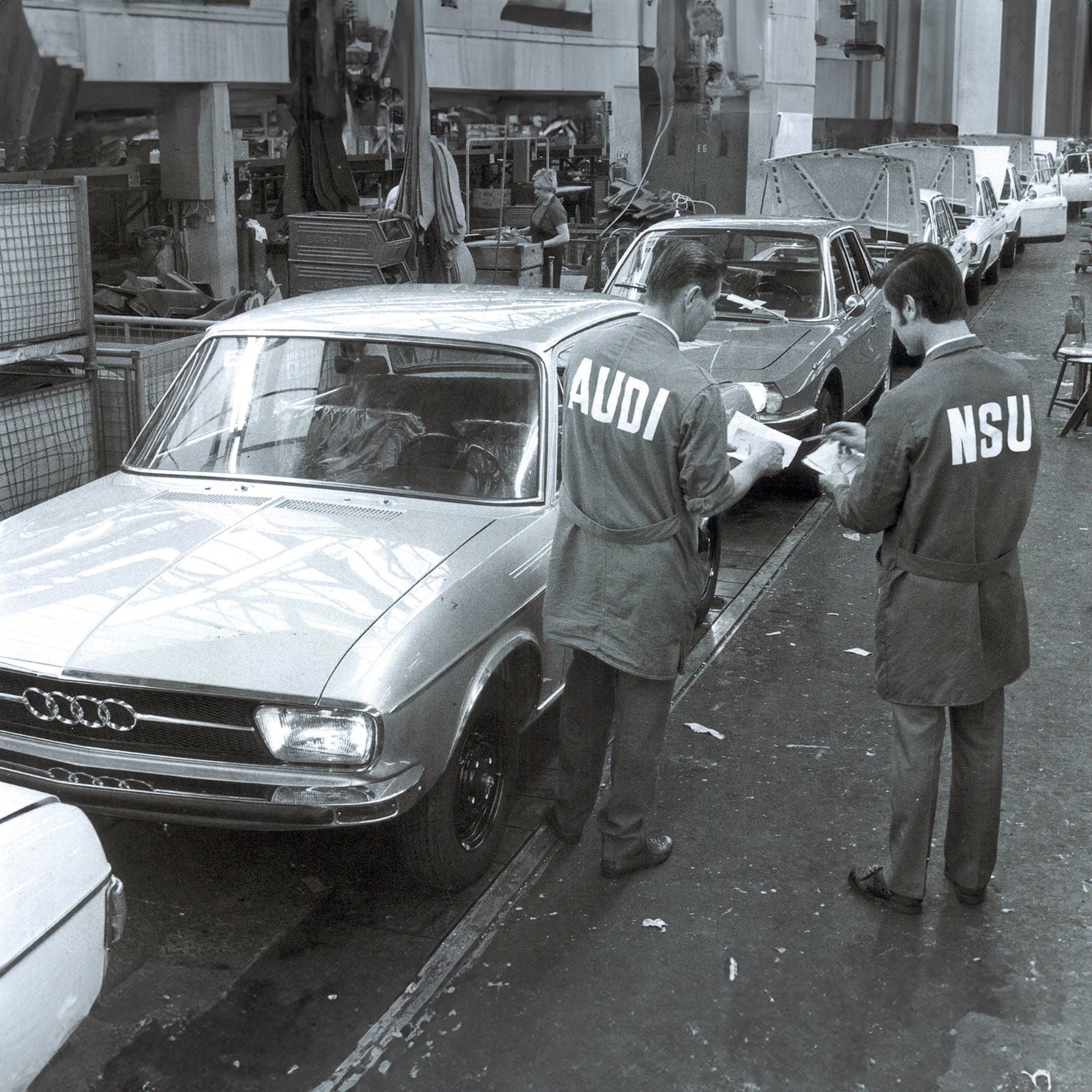 Two employees stand in front of a row of vehicles in the production hall