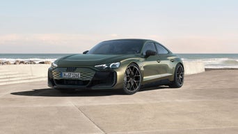 A sleek green Audi sedan parked by the seaside, showcasing modern design and sporty features against a clear sky and ocean backdrop.