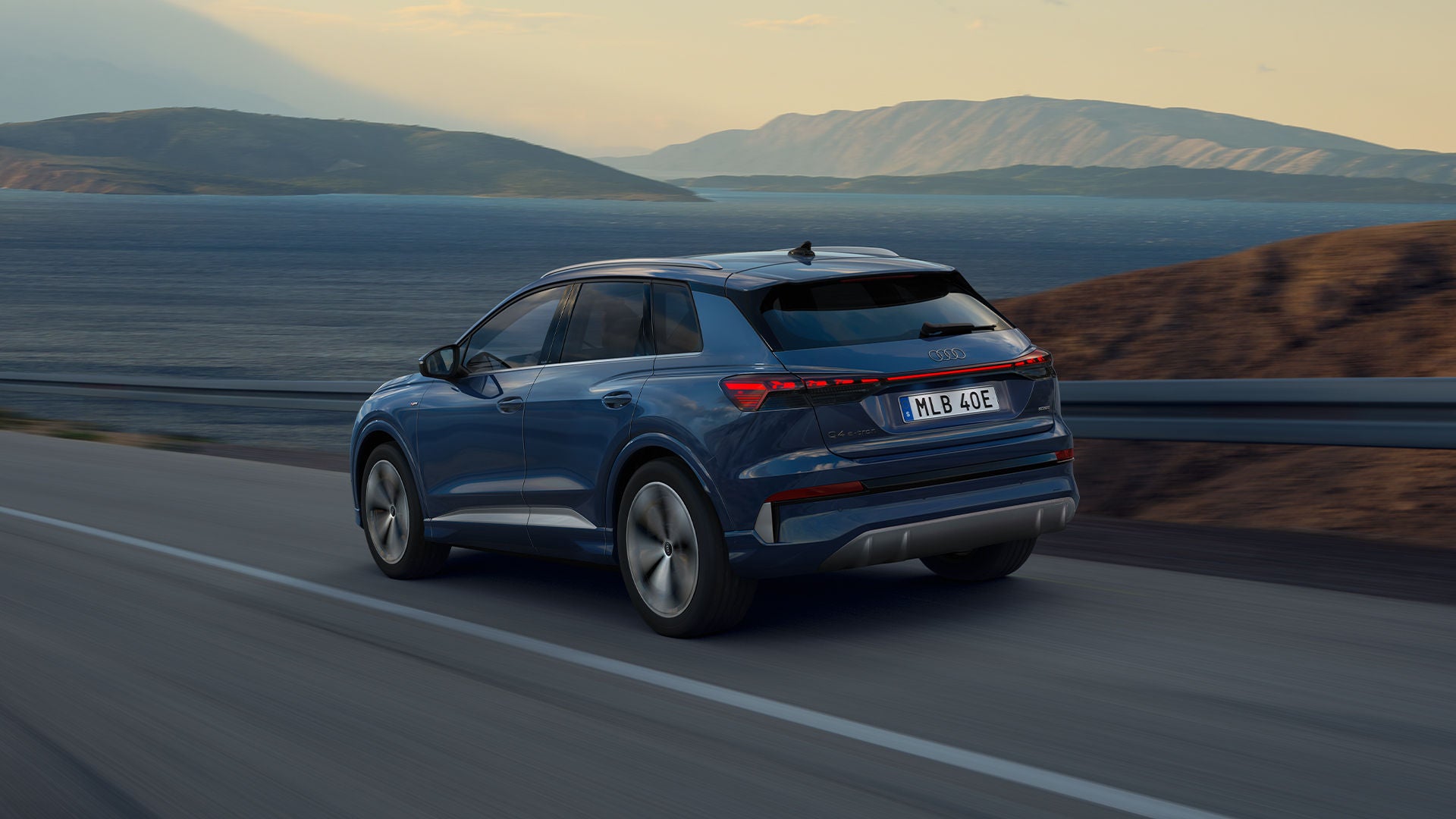 Q4 e-tron SUV sedd bakifrån på en slingrande bergsväg på natten, med havet till höger. I det mötande körfältet syns strålkastarna från mötande fordon.