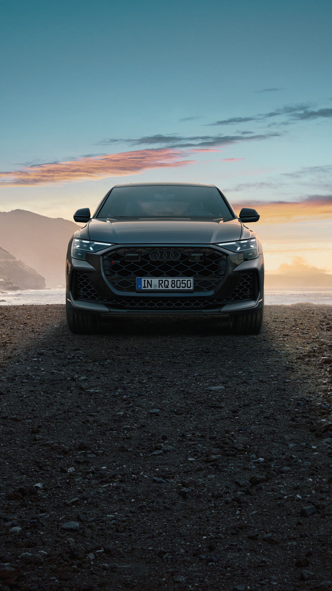 Der RS Q8 SUV von vorn an einem Strand auf Schotter, im Hintergrund das Meer und seitlich hervorragende Berge. Links ist ein Hotelkomplex zu erkennen.