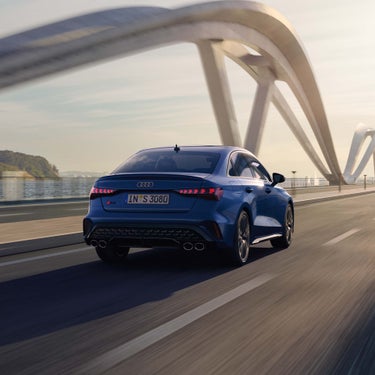 Heckansicht eines blauen Audi S3 Limousine auf einer Brücke bei Sonnenuntergang.