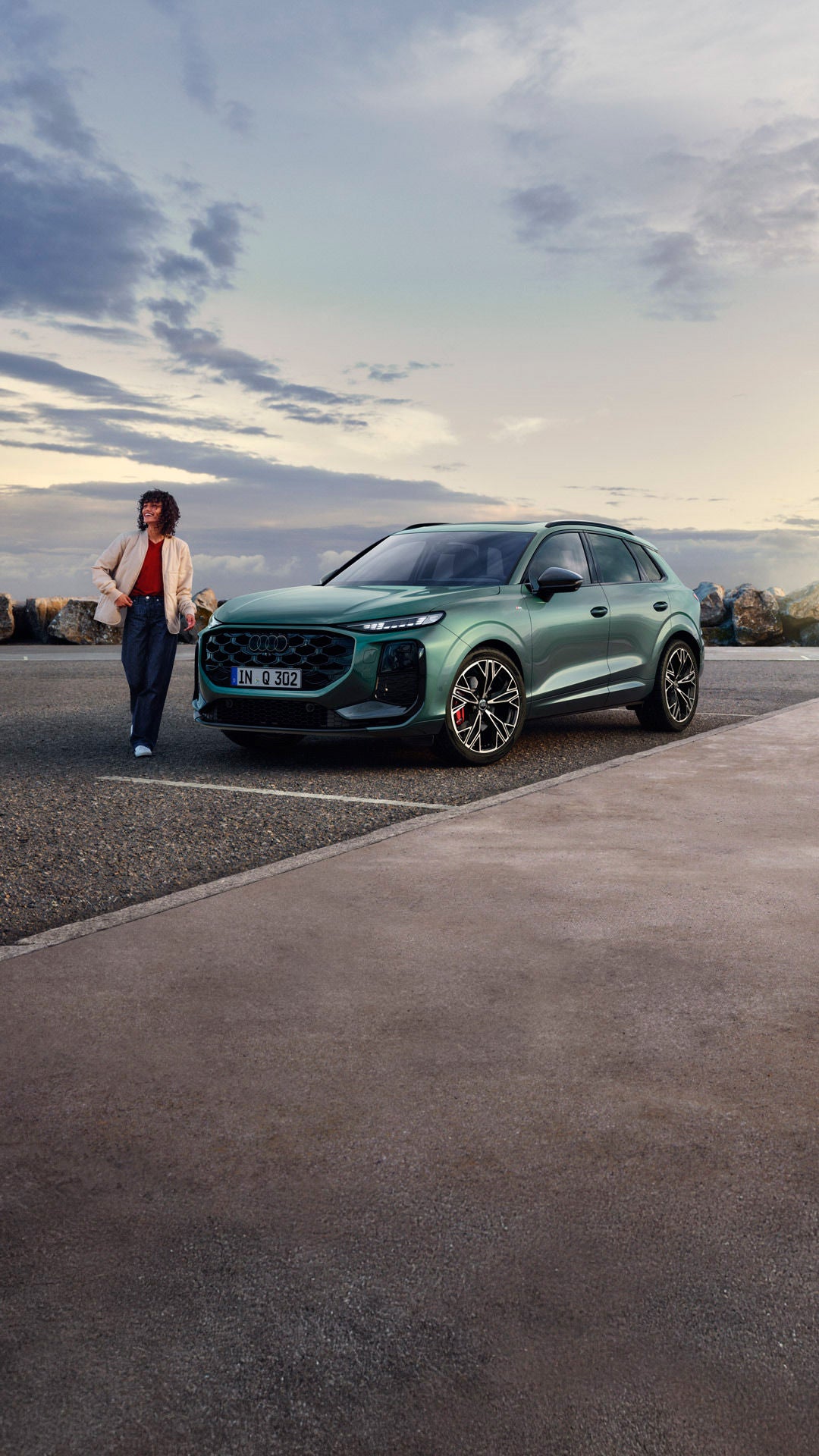 Vista lateral del Q3SUV estacionado en una carretera costera, con una mujer joven parada a su lado.