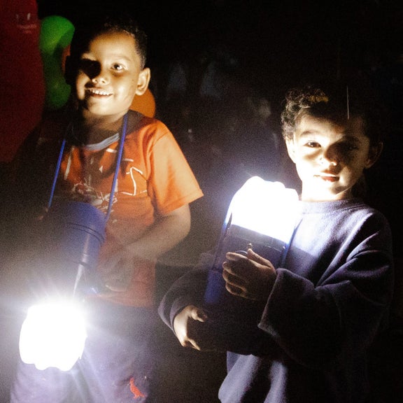 zwei Kinder gehen mit zwei Solarlaternen in der Hand durch die Dunkelheit.