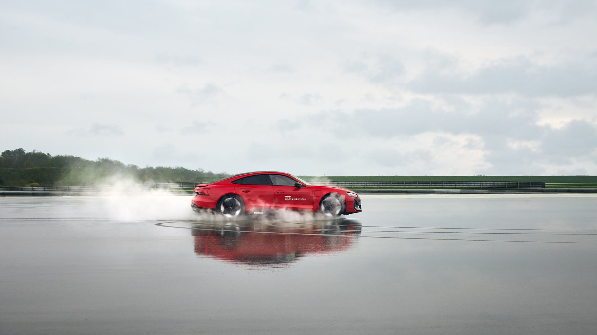 Roter Audi RS e-tron GT performance (Seitenansicht) fährt durch eine große Pfütze auf einem Übungsgelände. 