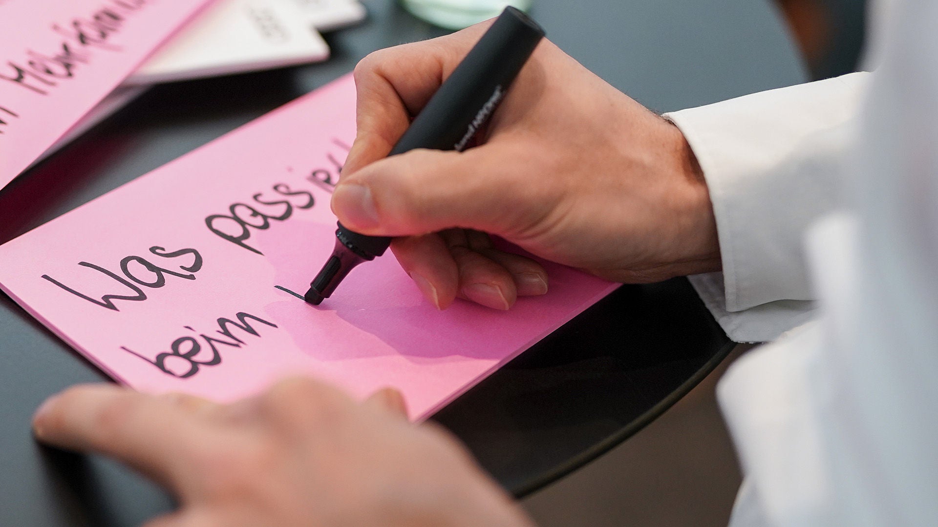 Eine Hand schreib mit schwarzem Edding einen Satz auf pinkes Papier