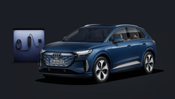 Der Q4 SUV e-tron schräg von vorn auf dunklem Hintergrund, dahinter eine moderne Ladesäule.