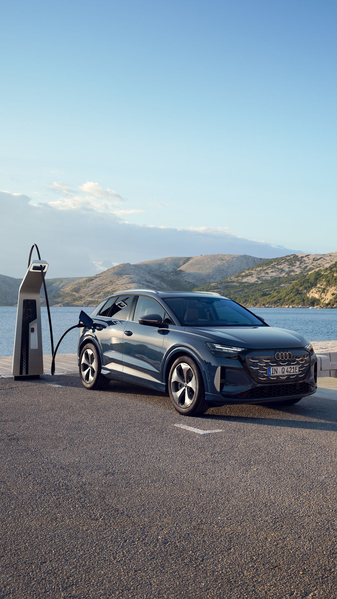 De nieuwe Q4 e-tron staat aan een laadpaal met op de achtergrond een groot meer.