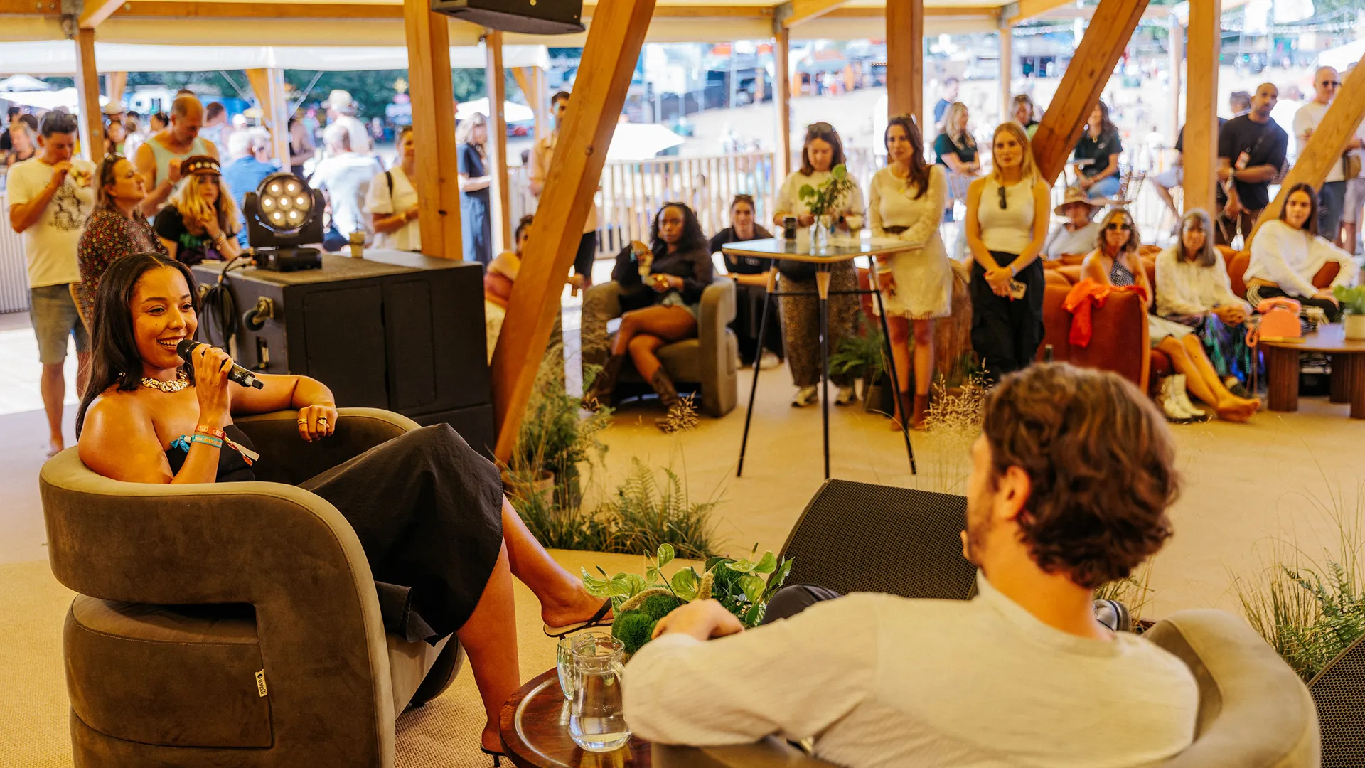 A group sits around a low wooden table topped with dried floral arrangements and drinks, relaxing on cushioned seating in a lounge area. A group sits around a low wooden table topped with dried floral arrangements and drinks, relaxing on cushioned seating in a lounge area.