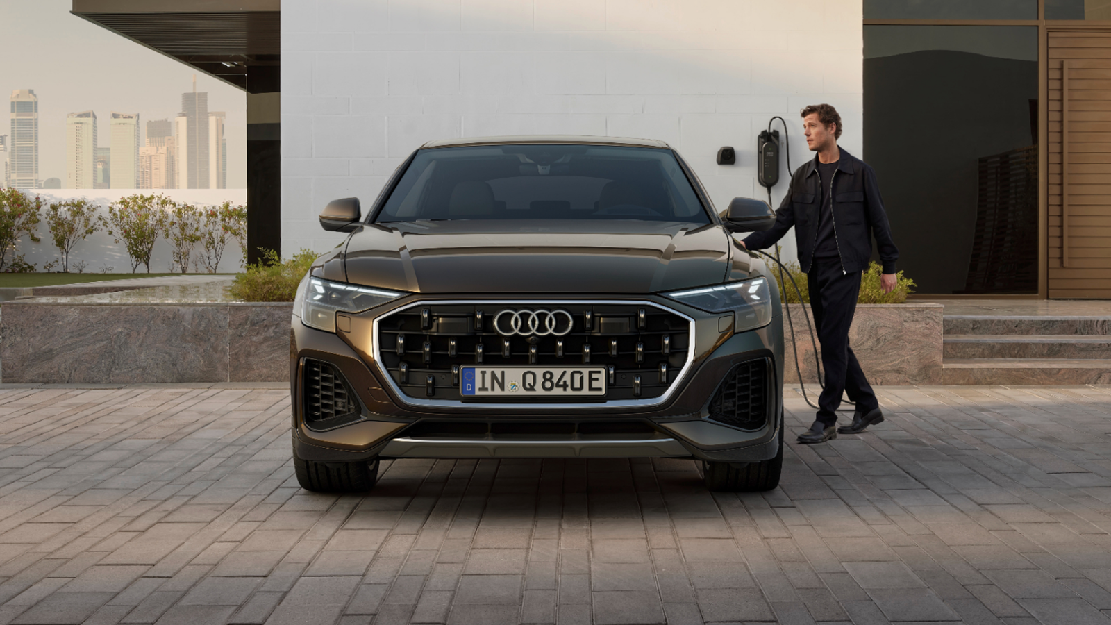 A black Audi Q8 TFSI e in front of an EV charger and man standing on the right