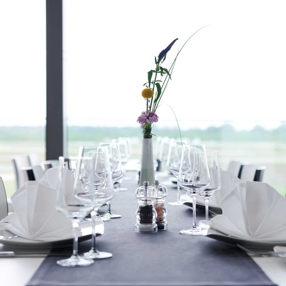 Nahaufnahme eines festlich gedeckten Tisches mit weißen Servietten, Gläsern und einer einzelnen Blumenvase in der Mitte.