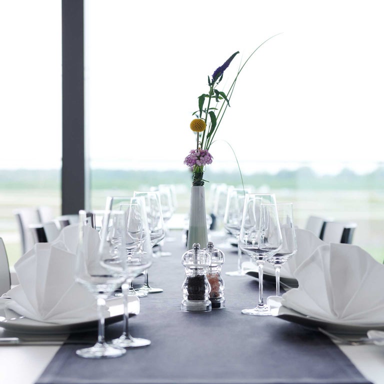 Nahaufnahme eines festlich gedeckten Tisches mit weißen Servietten, Gläsern und einer einzelnen Blumenvase in der Mitte.