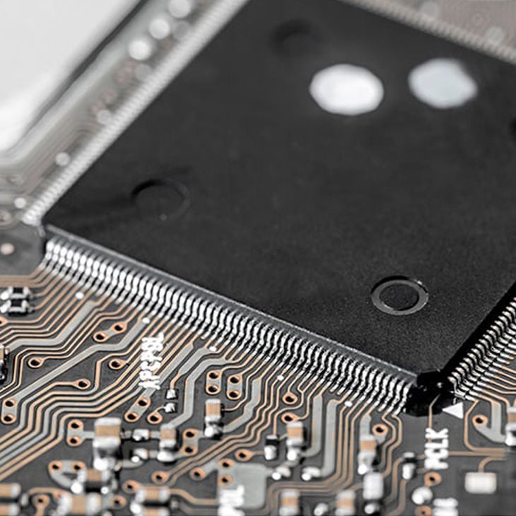 Makroaufnahme einer Leiterplatte mit feinen Leiterbahnen und angeschlossenem schwarzen Mikrochip.