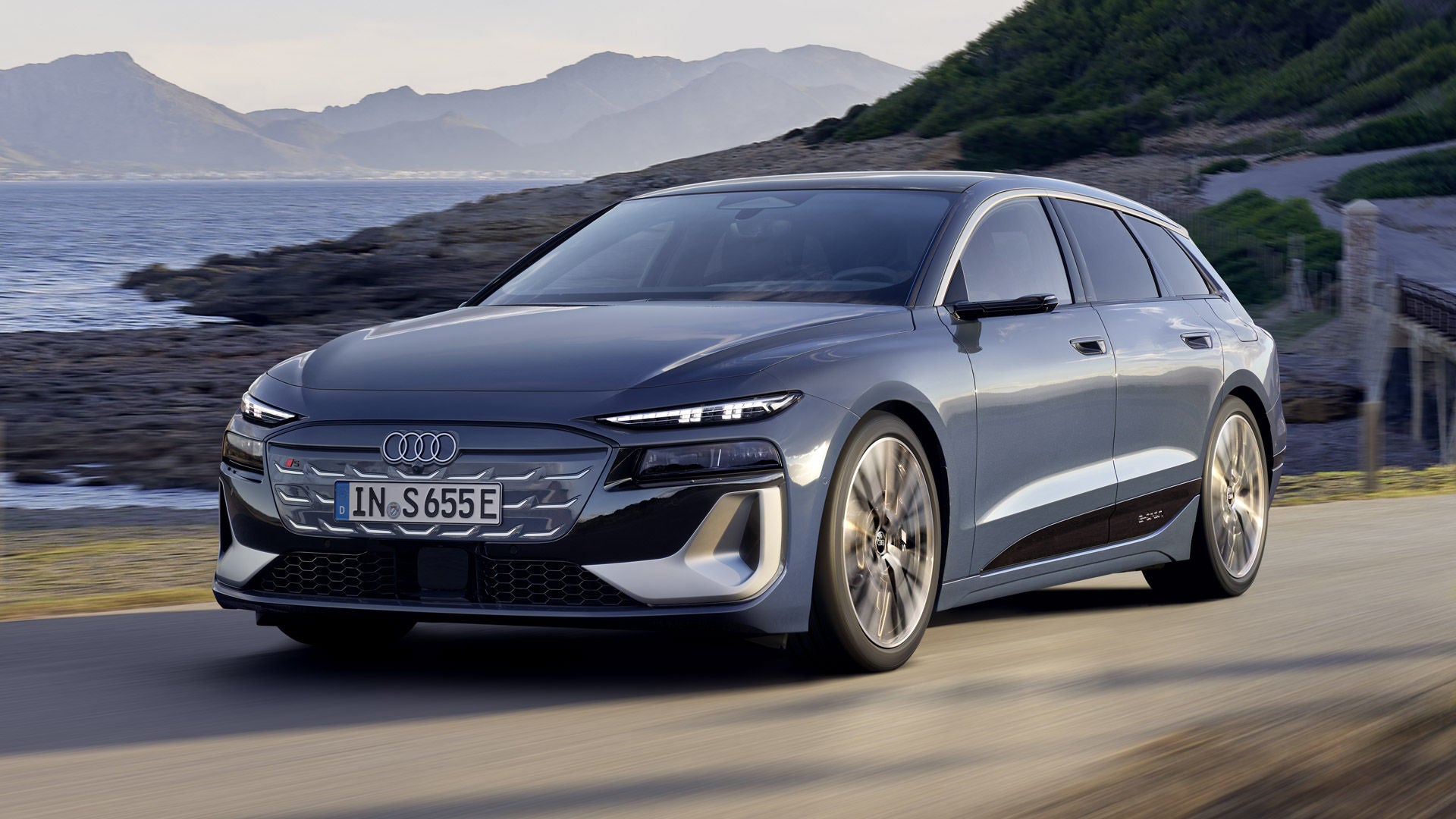 The S6 Avant e-tron seen from an angle as it drives along a coastal road. Mountains can be seen in the background.