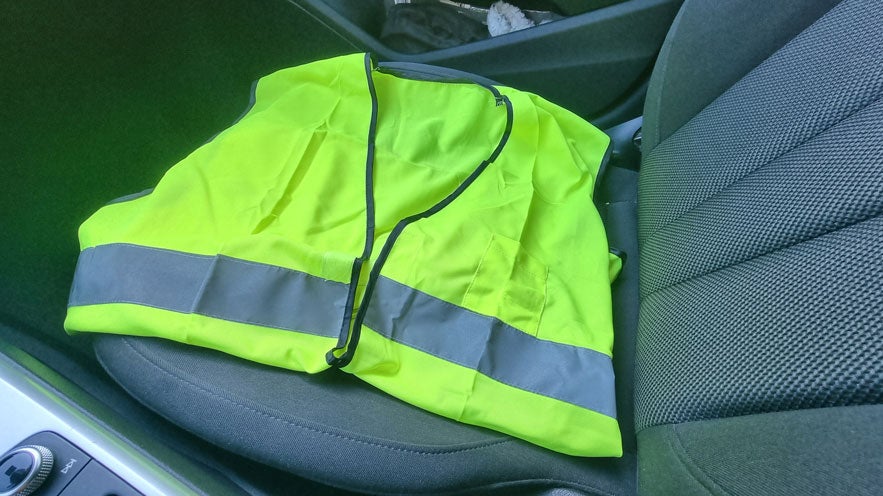 Leuchtgelbe Warnweste mit reflektierendem Streifen liegt auf einem Autositz im Innenraum.