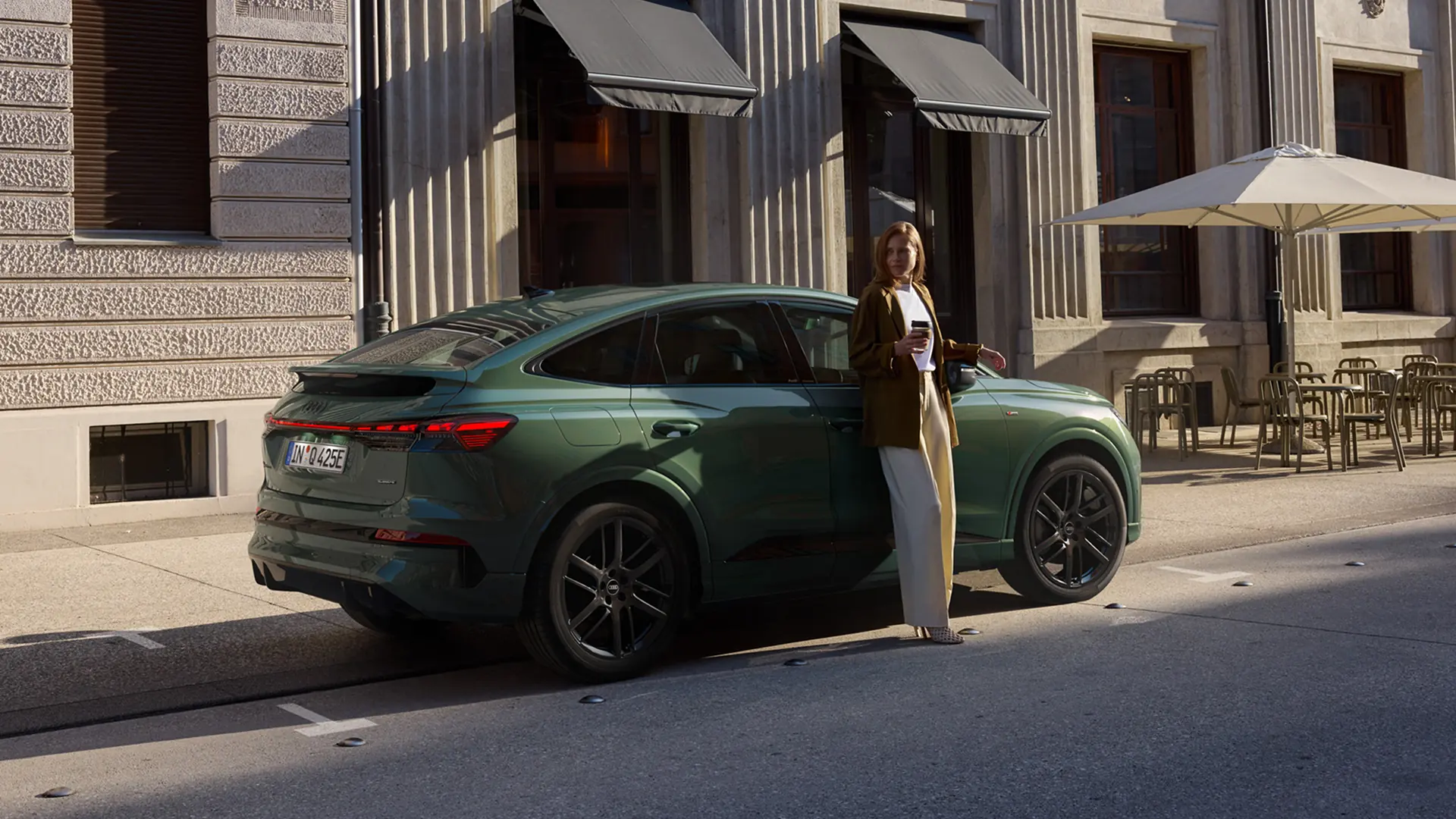 Woman standing beside a green Audi Q4 Sportback e-tron car on a city road.