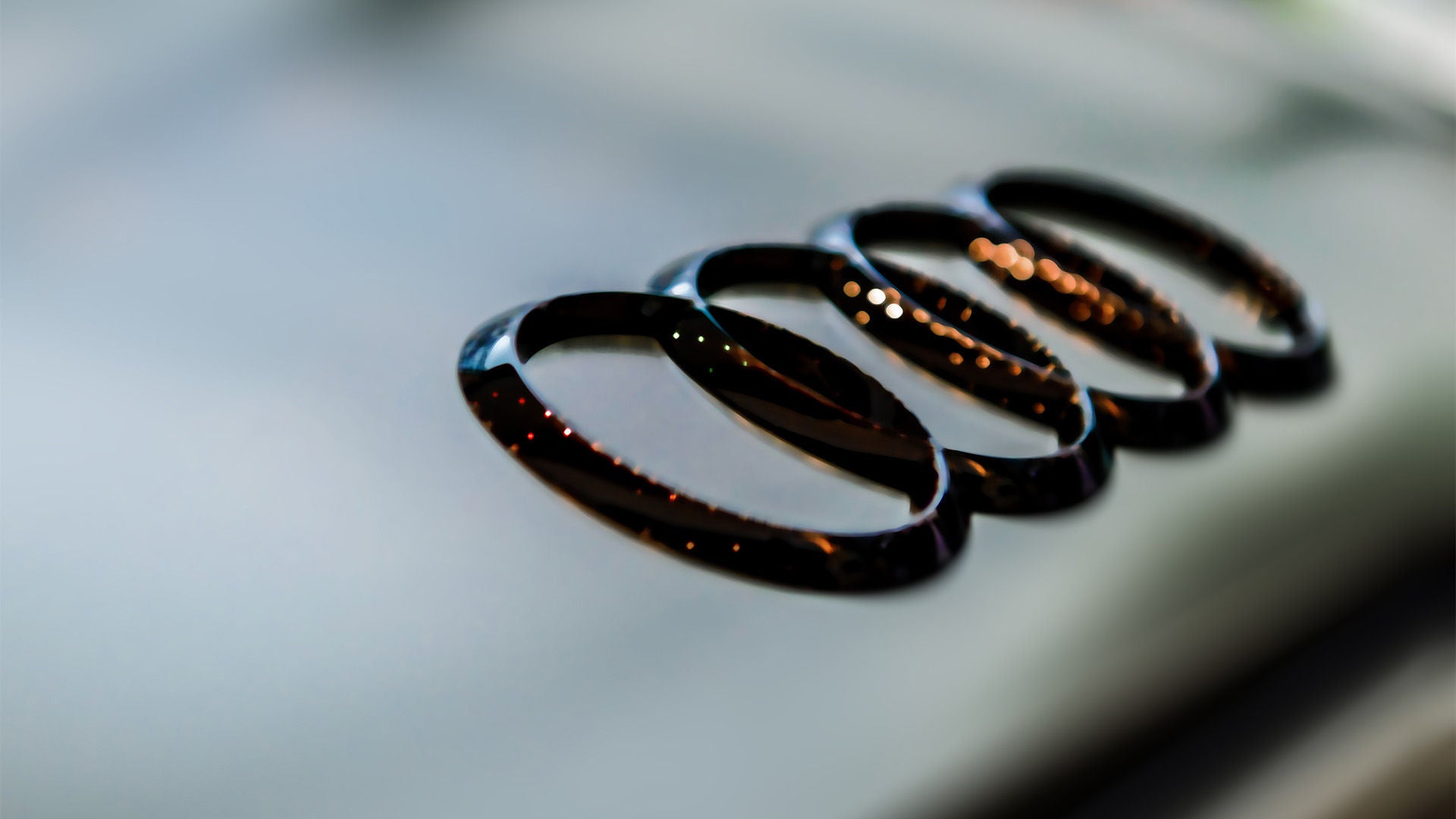 Nahaufnahme des glänzenden schwarzen Audi-Logos mit vier Ringen auf verschwommenem Hintergrund.