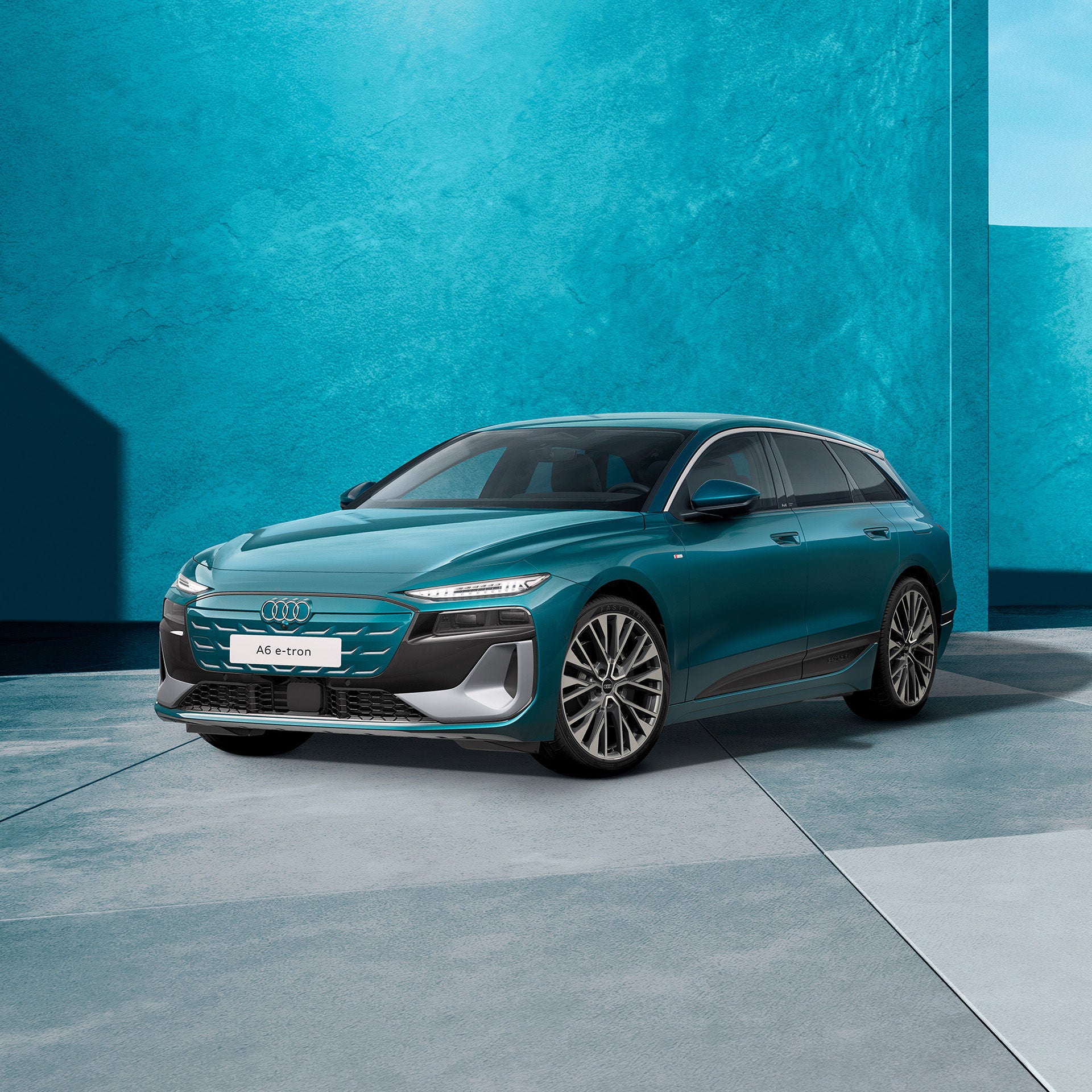 Ein türkisfarbener Audi A6 Avant e-tron von schräg vorne fotografiert vor einer modernen Kulisse. 