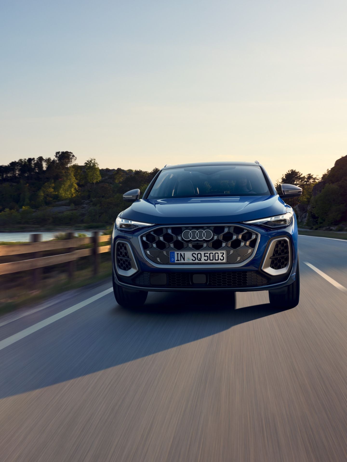 A blue SUV driving on a highway with a scenic backdrop during sunset.
