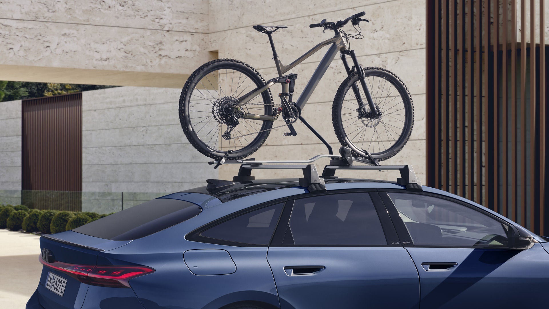 Der A6 Sportback e-tron im Anschnitt vor einem modernen Haus. Auf dem Dachgepäckträger ist ein Mountain Bike festgezurrrt.&nbsp;