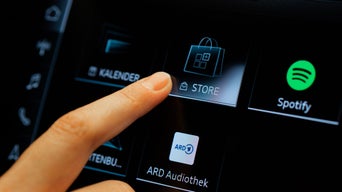 Finger tippt auf das Store-Symbol im Audi-Fahrzeugdisplay neben Apps wie Spotify und ARD Audiothek.