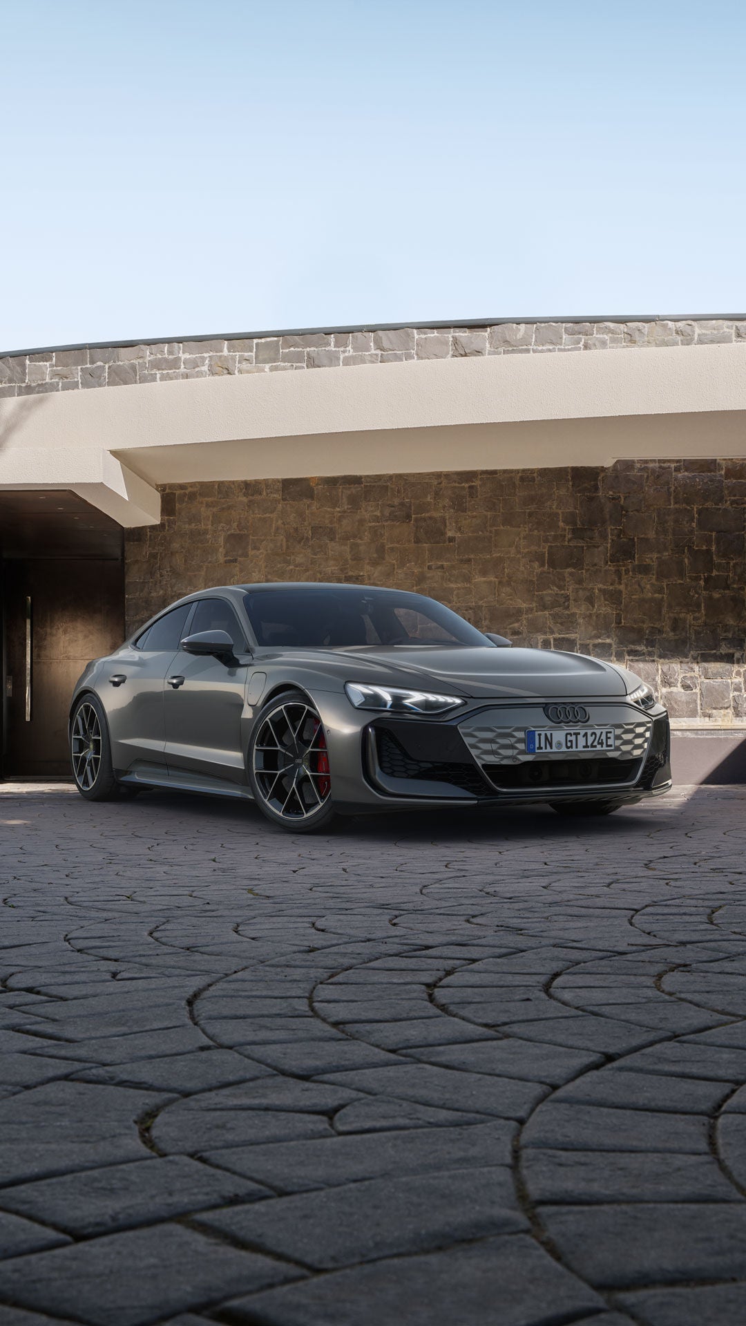 Grauer Audi e-tron GT steht auf gepflasterter Einfahrt vor einem modernen Haus mit Stein- und Putzfassade.