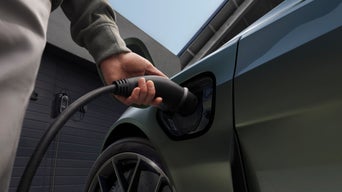 A hand plugs a charging cable into the electric vehicle's port, showcasing modern charging infrastructure and a sleek car design.