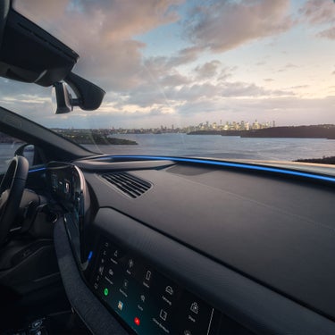 Cockpit eines Audi Q6 Sportback e-tron mit digitalem Display, Blick durch die Frontscheibe auf eine erleuchtete Stadt am Wasser.