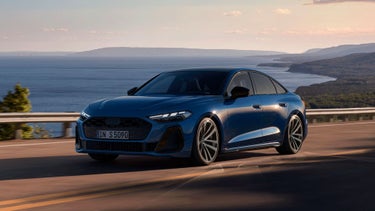 The dark blue S5 Saloon drives along a road by the coast.