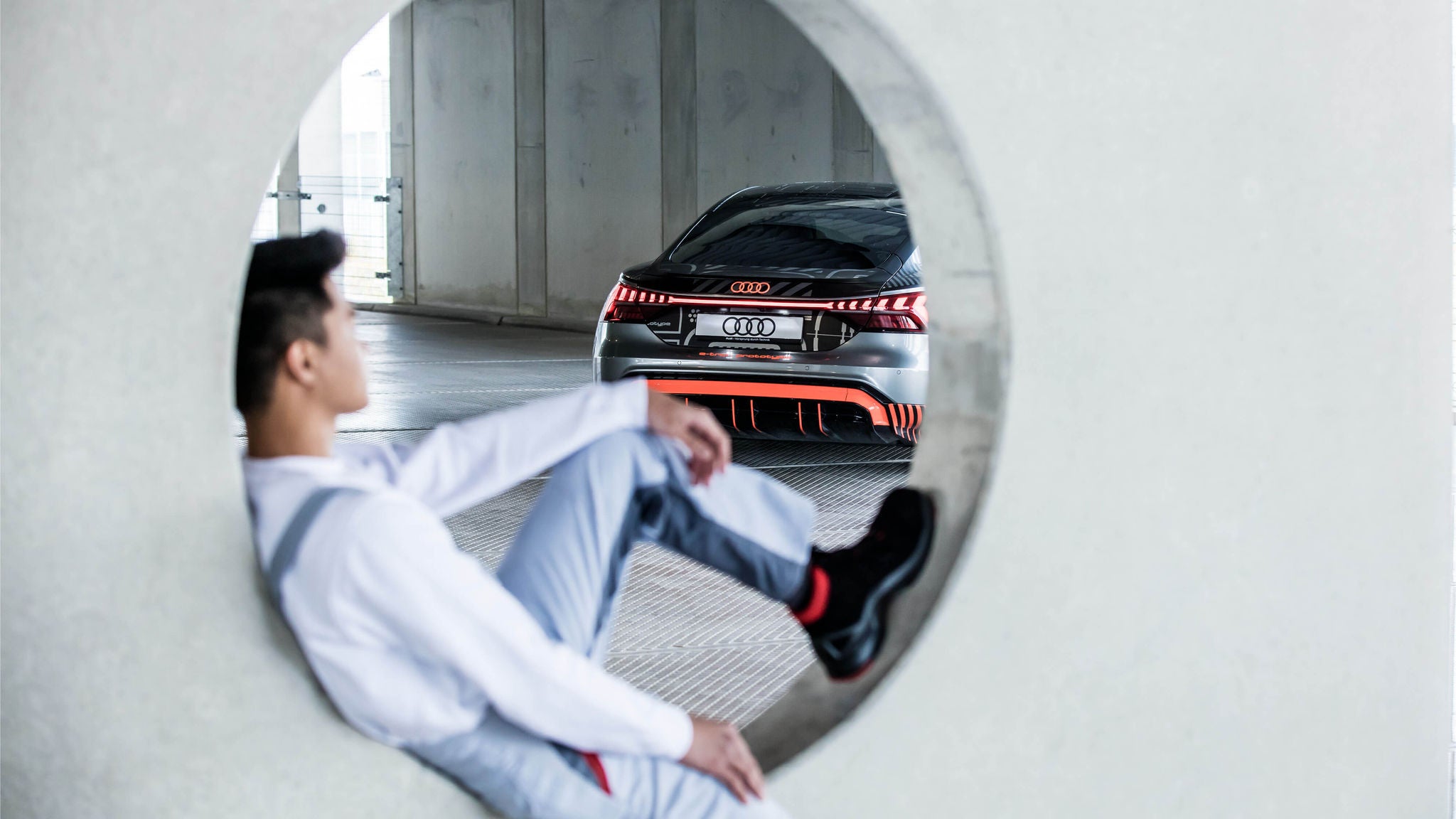 Mann sitzt in Betonöffnung und blickt auf parkenden Audi mit leuchtendem Rücklicht.