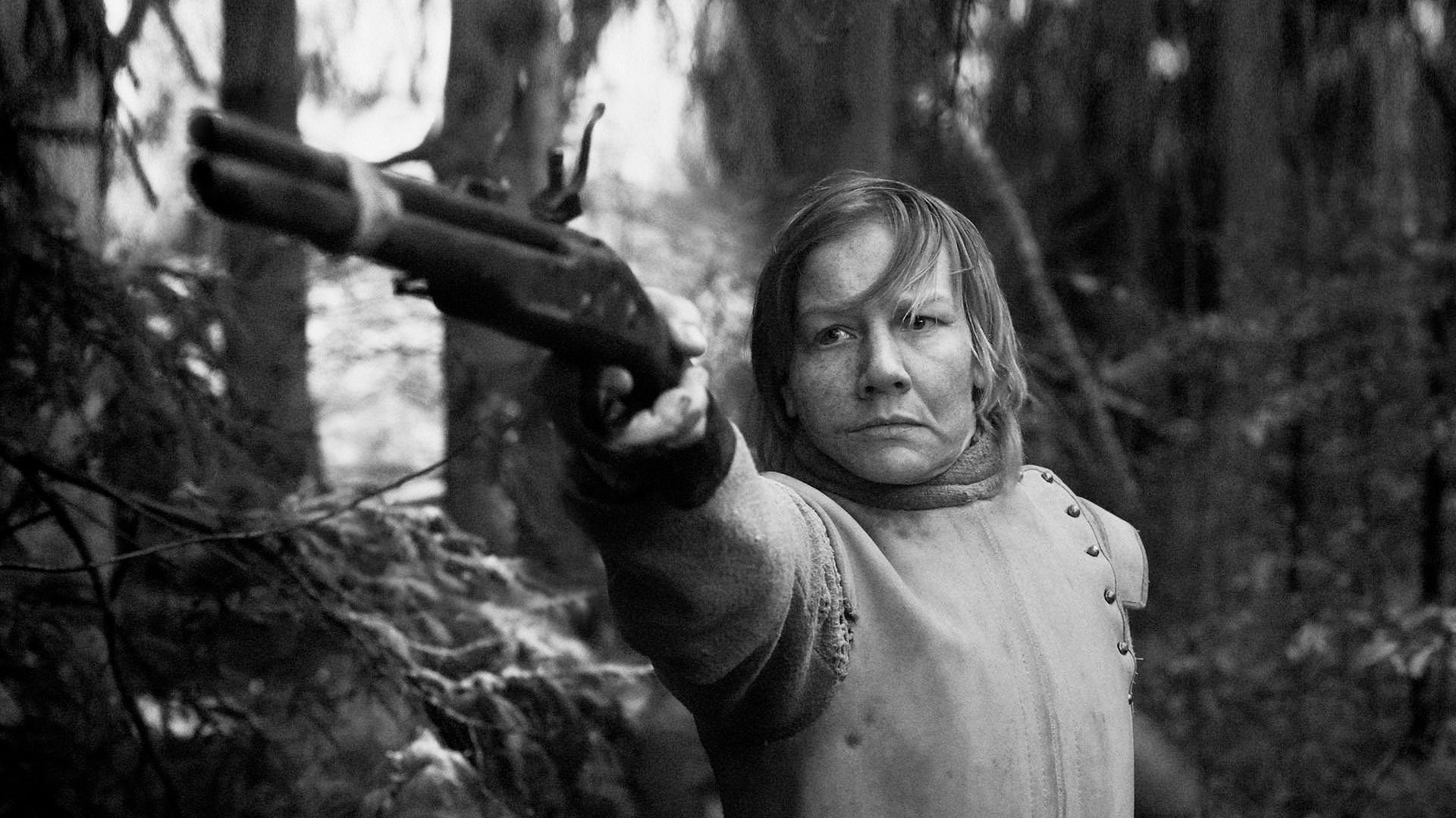 Ein Fremder - gespielt von Sandra Hüller - zielt mit einer historischen Waffe auf etwas im Wald.