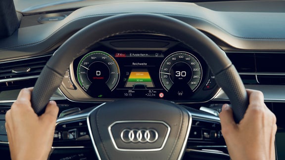 Driver's view of an Audi steering wheel and digital dashboard displaying vehicle information.
