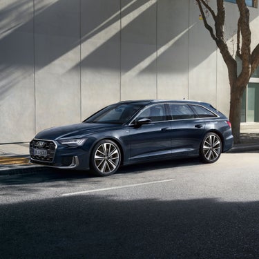 Dark blue Audi car parked on a city street with sunlight casting shadows on a wall behind.