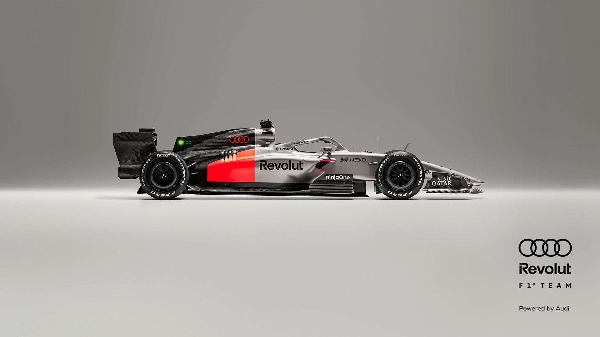 Seitenansicht eines silber-schwarzen Formel-1-Rennwagens mit roten Akzenten vor grauem Hintergrund, Audi- und Revolut-Logo in schwarz am Rand.