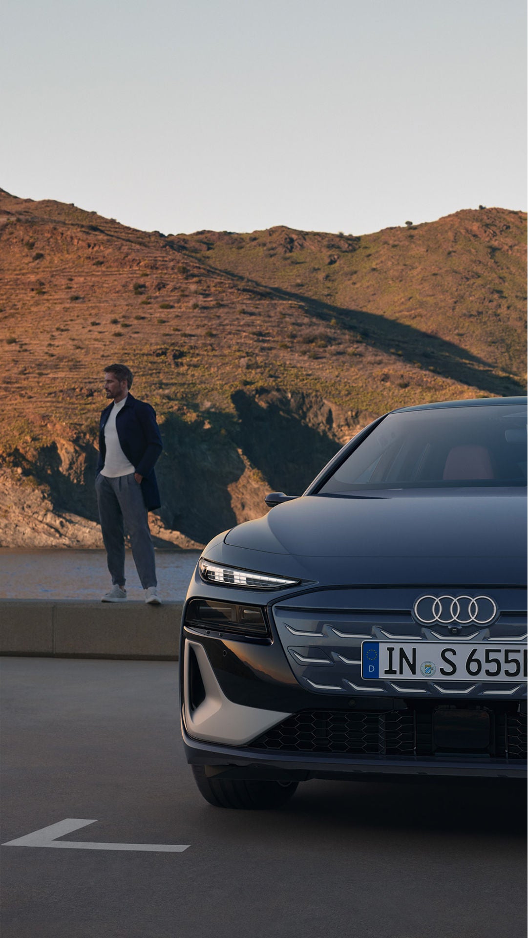 An Audi S6 Avant e-tron parked in front of a mountain with a man standing at the back