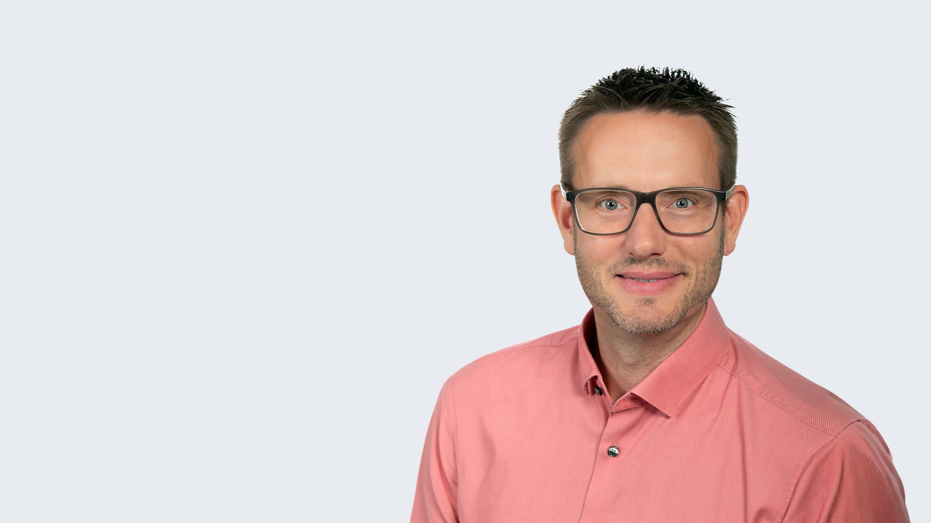 Magnus Weiß: Porträt eines Mannes mit Brille und rosafarbenem Hemd vor hellgrauem Hintergrund.