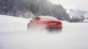 A red Audi RS e-tron GT performance is driving along a snow-covered track; snow kicked up by the tyres is partially obscuring the rear of the car. 