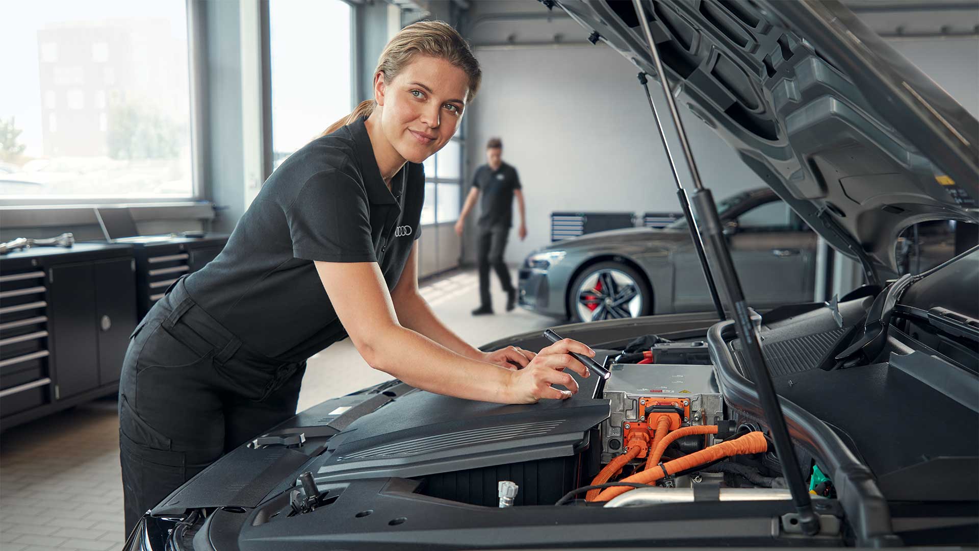 Audi Mitarbeiterin inspiziert Fahrzeug bei offener Motorhaube in der Werkstatt