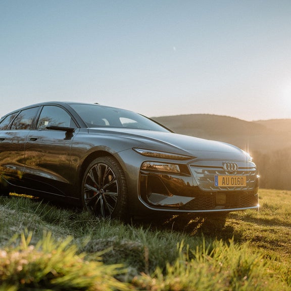 Audi A6 e-tron steht auf grüner Wiese und die aufgehende Sonne spiegelt sich auf der Motorhaube.