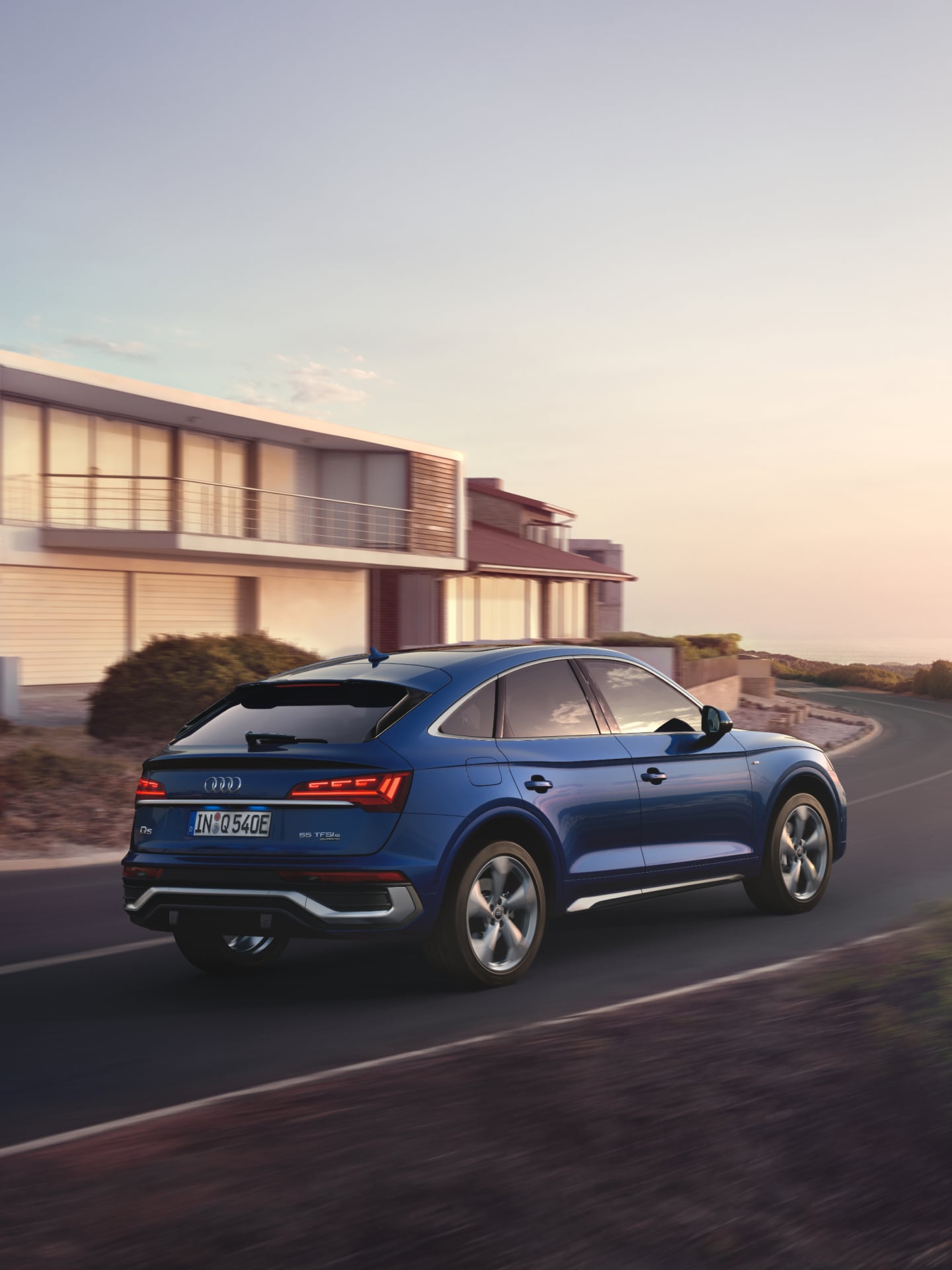 Blue SUV driving on coastal road at sunset.