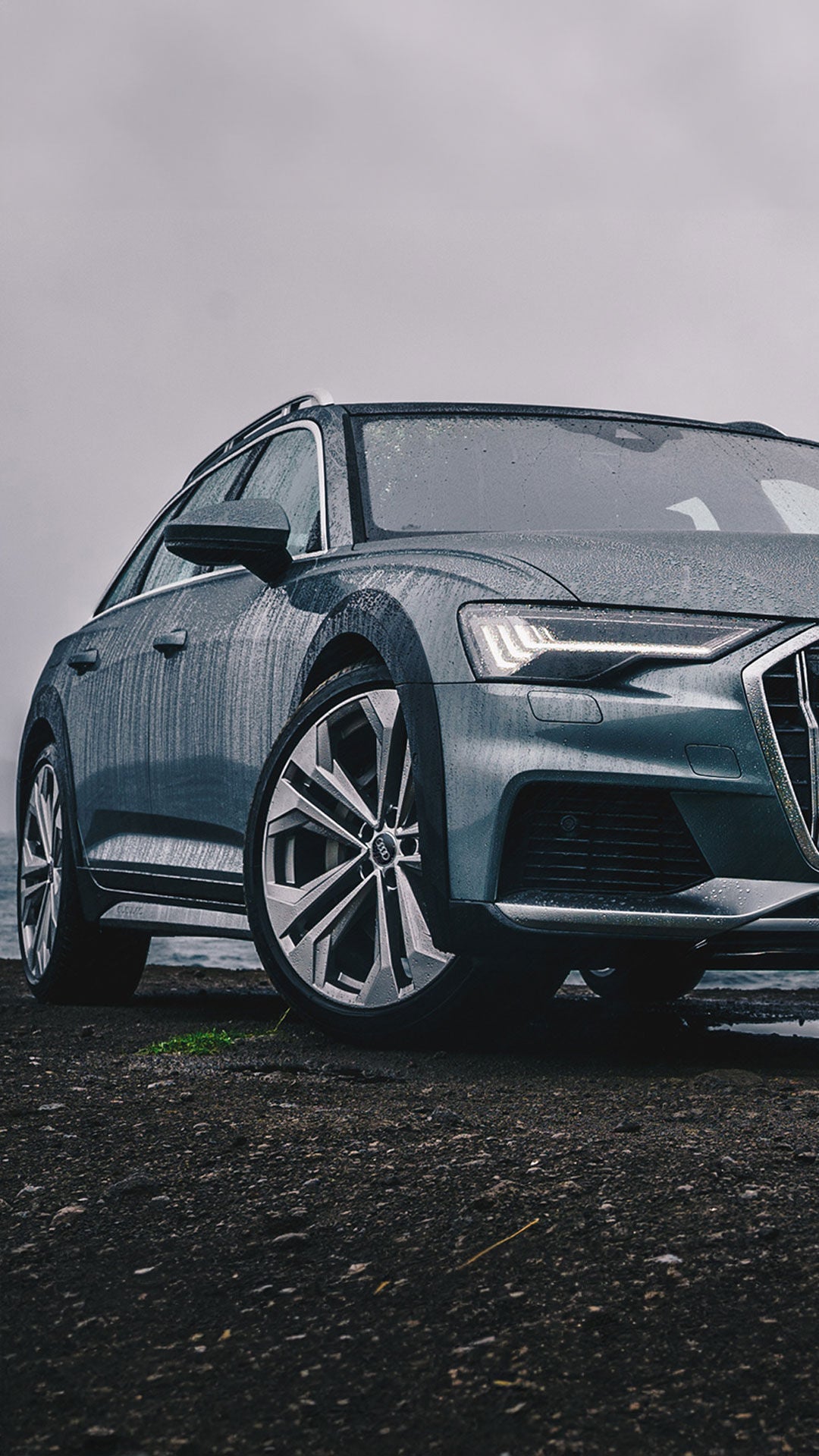 Audi A6 bei nassem Wetter am Wasser geparkt, Nahaufnahme von schräg vorne mit eingeschaltetem LED-Tagfahrlicht.