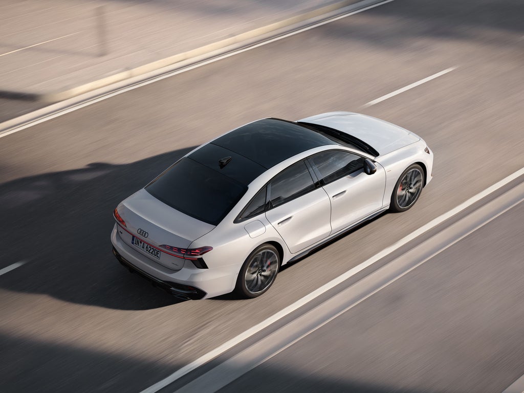 The white A6 Saloon e-hybrid is driving along a road in an urban setting, viewed from a high angle.