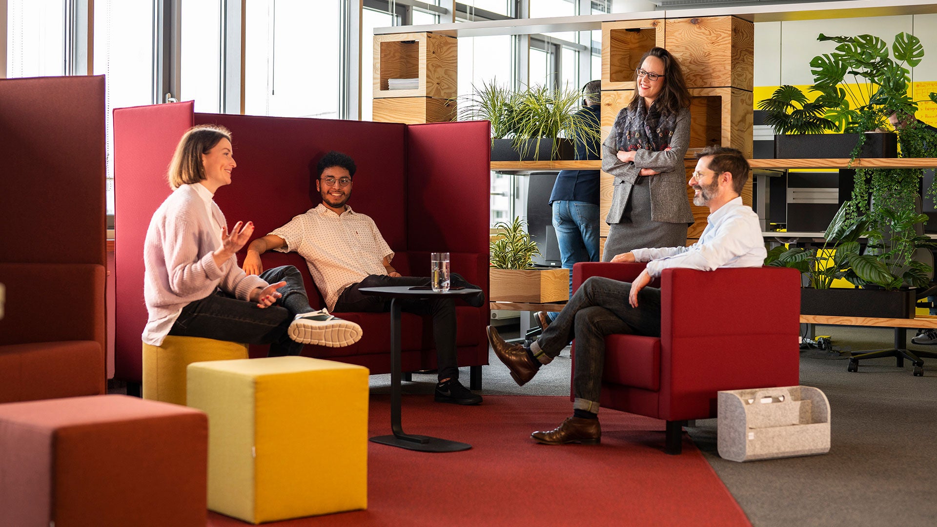 Drei Personen sitzen und eine steht. Sie sind im Gespräch