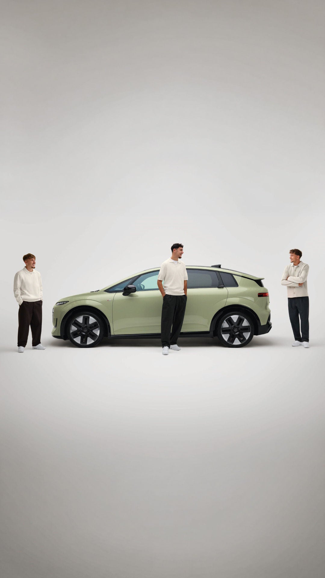 Hellgrüner Audi A2 e-tron in Seitenansicht auf hellem Studiogrund; drei Männer in heller Kleidung stehen davor.