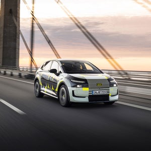 Oblique front view of the Audi A2 e-tron with yellowish wrap as it drives over a bridge.
