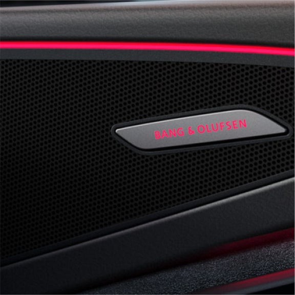 Close-up of a car speaker grille featuring a Bang & Olufsen logo illuminated by a subtle red light.