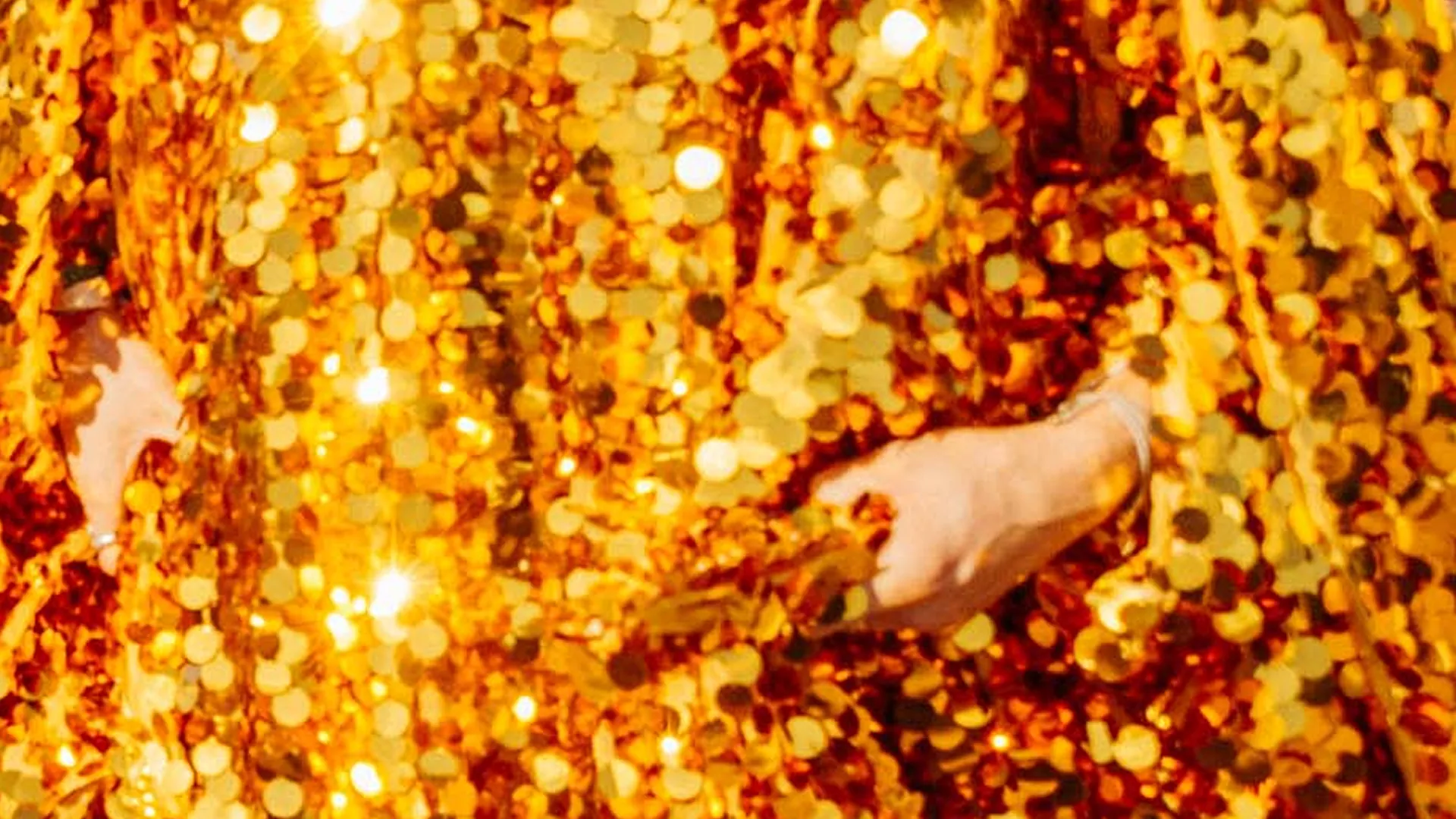 Close-up of hands reaching through a shimmering gold sequinned costume or backdrop, catching the light. Close-up of hands reaching through a shimmering gold sequinned costume or backdrop, catching the light.