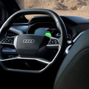 Close-up of an Audi steering wheel with modern controls and a minimalistic dashboard displaying digital navigation and vehicle information.