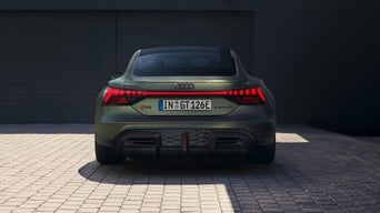 Rear view of an Audi RS e-tron GT in green, showcasing its sleek design and distinctive LED taillights against a dark backdrop.